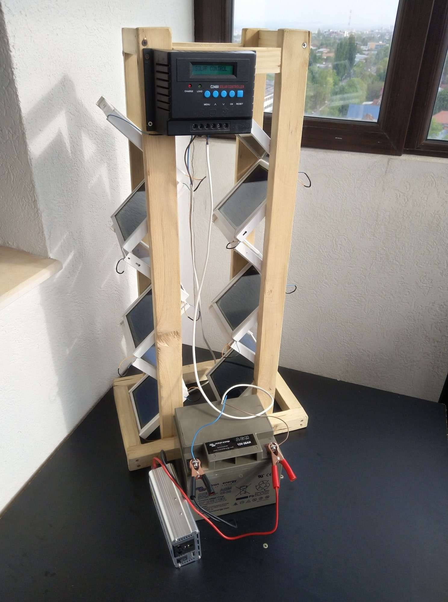 Small home-built solar test rig on a timber frame wired to a charge controller, a 12V battery and a compact inverter